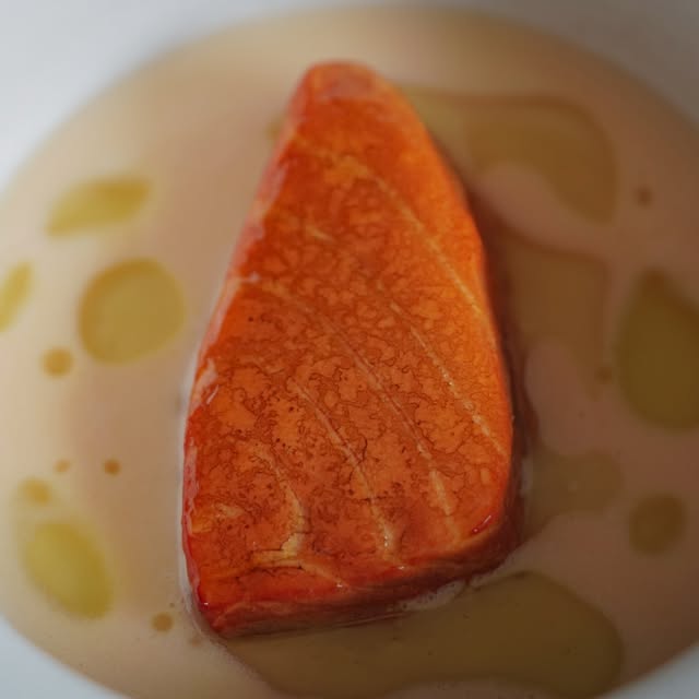 A cured fillet of fish resting in a pale broth dotted with oil