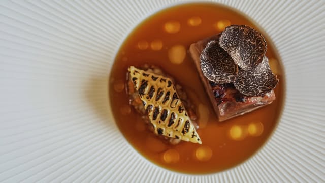 A composed course with shaved black truffle over a broth, on a ribbed white plate